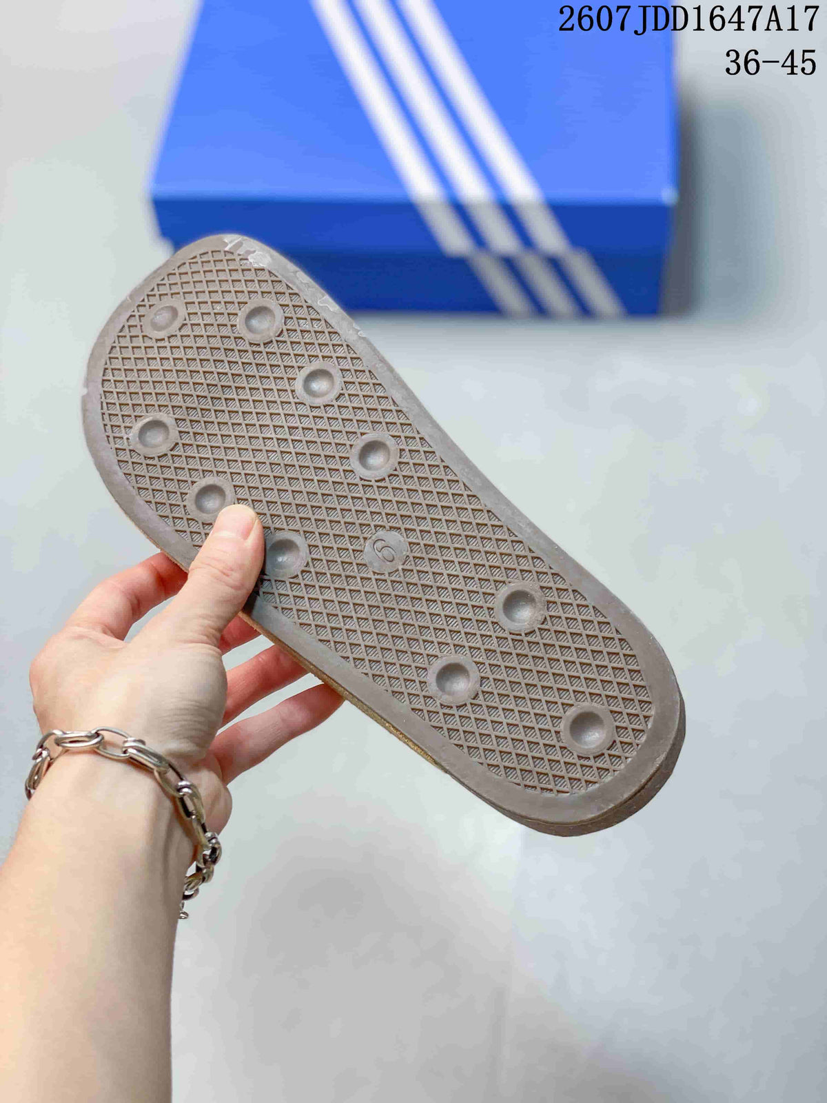 Underside view of a beige mule sandal showing the textured outsole and circular tread details, with a blue adidas shoe box in the background.