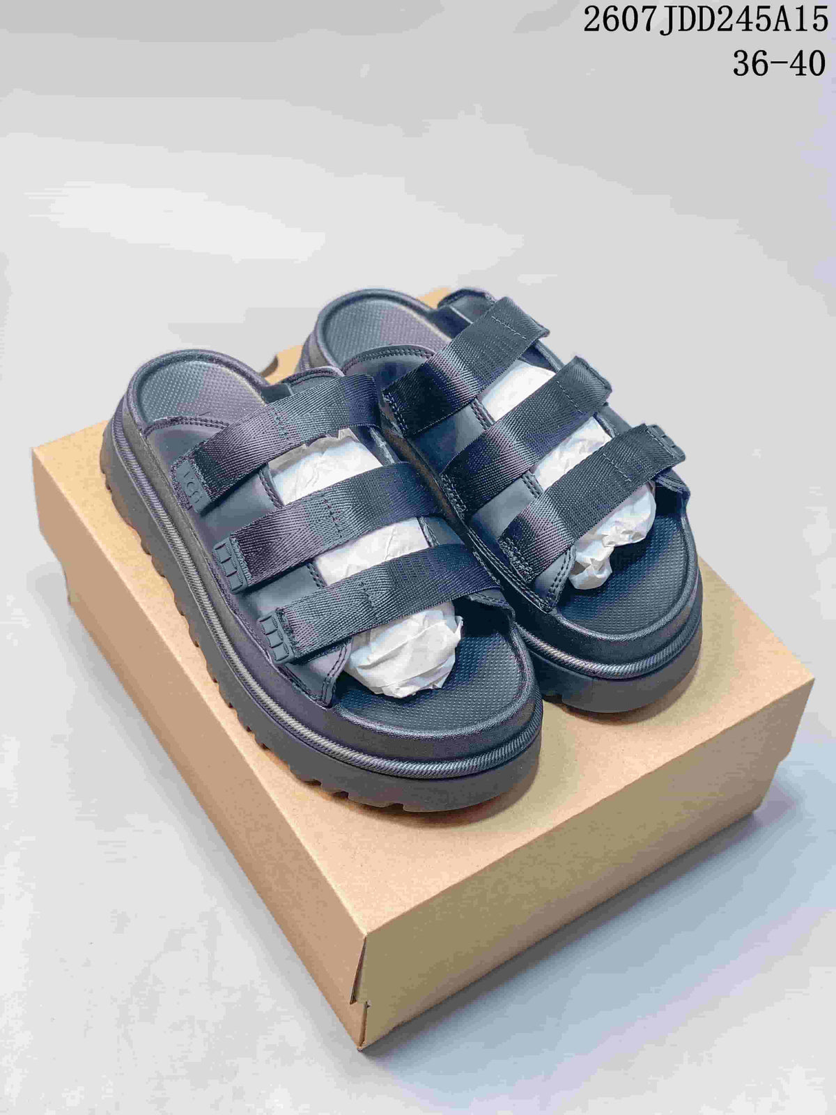 Pair of black UGG GoldenGlow platform slide sandals shown on a box, with three adjustable straps and a lugged outsole.