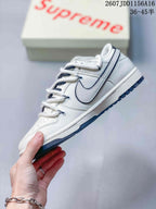 Side view of an off-white low-top sneaker with a layered Swoosh, dark blue trim and matching outsole.