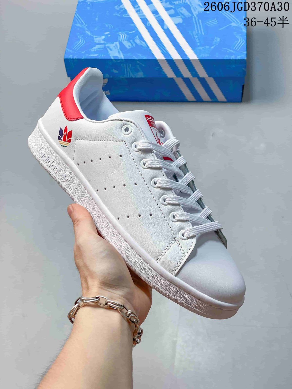 White Stan Smith-style sneaker with a multicolor heel emblem and a red heel tab.