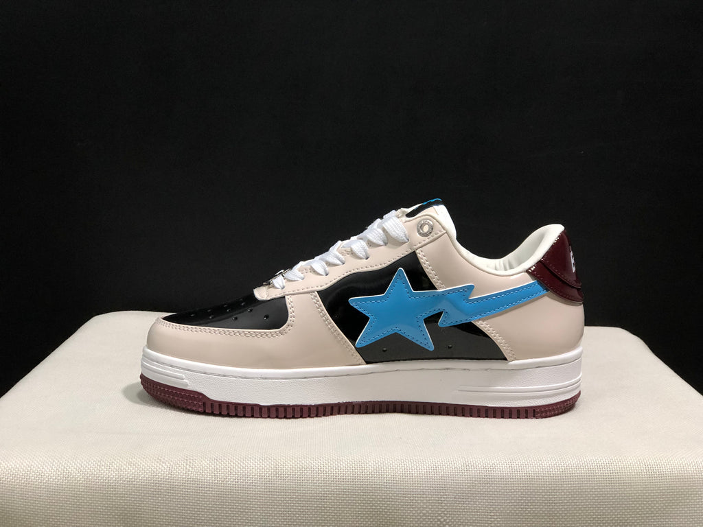 Profile view of one sneaker showing the cream upper, black toe and side panels, blue star emblem, white midsole, and burgundy outsole.