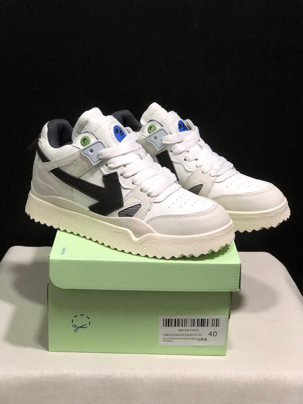 Pair of white sneakers with black arrow side details displayed on a light-green shoebox.