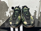 Front view of black BAPE STA sneakers with green and tan camouflage, patterned laces, and gold accents.