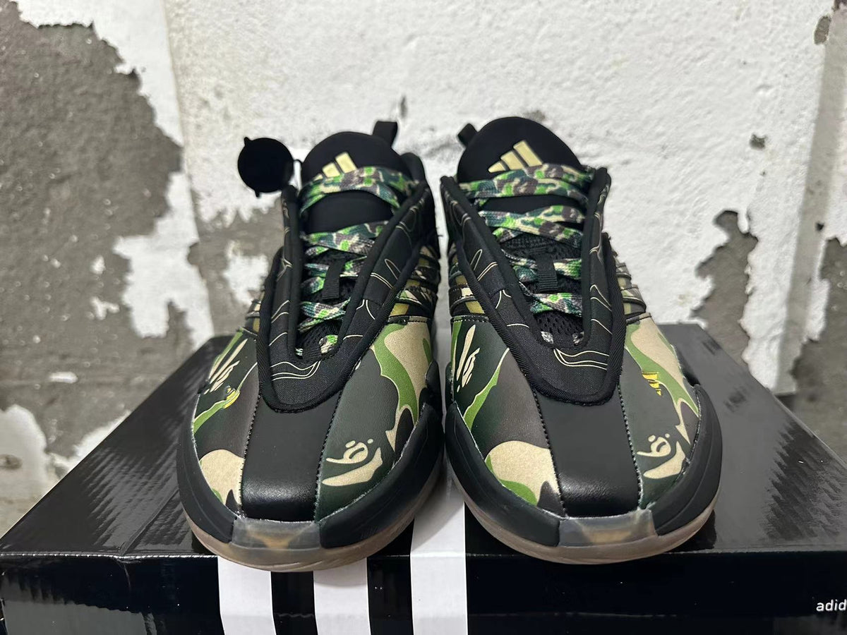 Front view of black BAPE STA sneakers with green and tan camouflage, patterned laces, and gold accents.