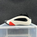 Side view of a cream, black, and red low-top sneaker on a display stand.