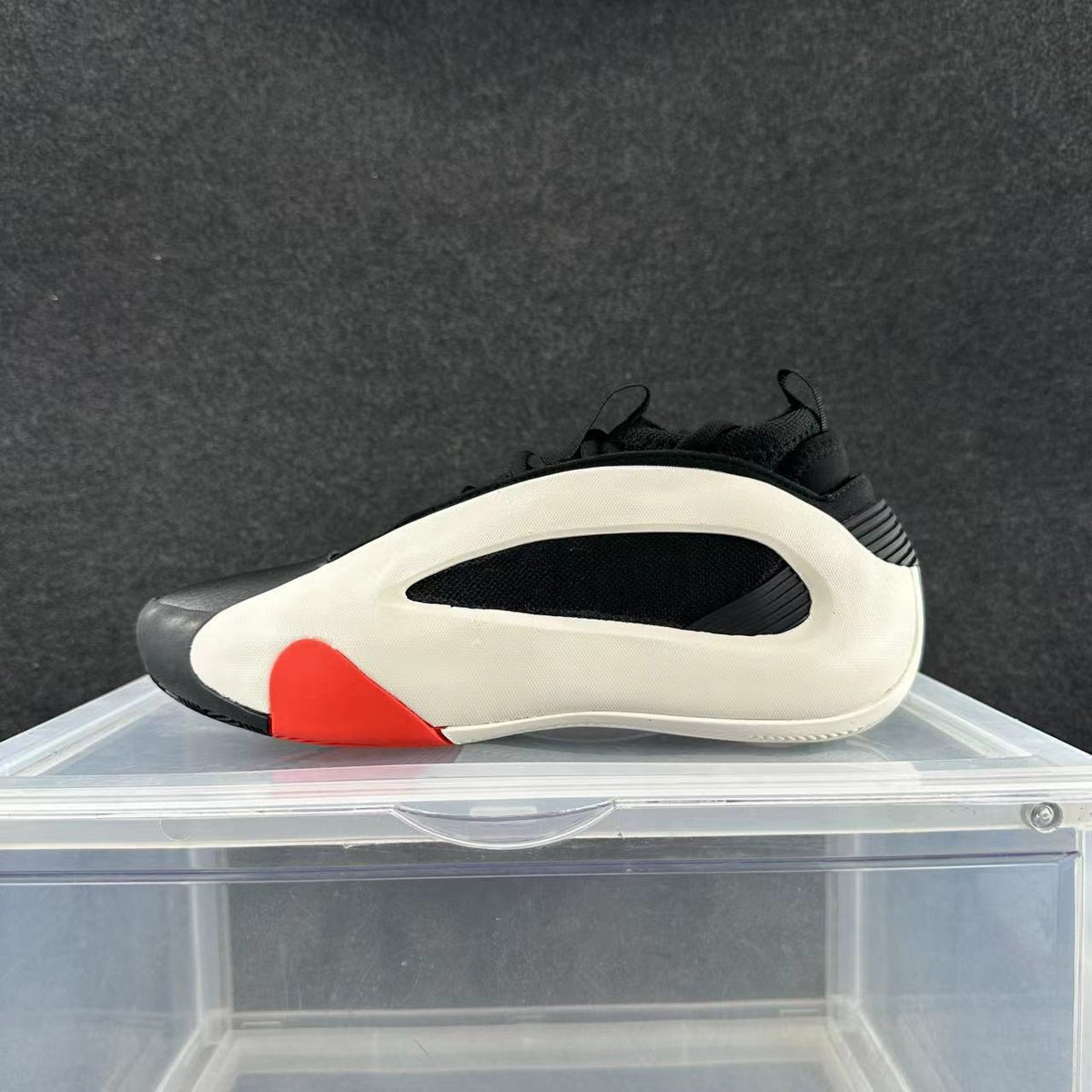 Side view of a cream, black, and red low-top sneaker on a display stand.