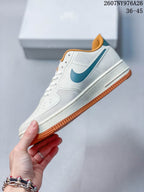 Side profile of the white low-top sneaker showing the teal Swoosh, layered panels, white midsole, and orange rubber outsole.