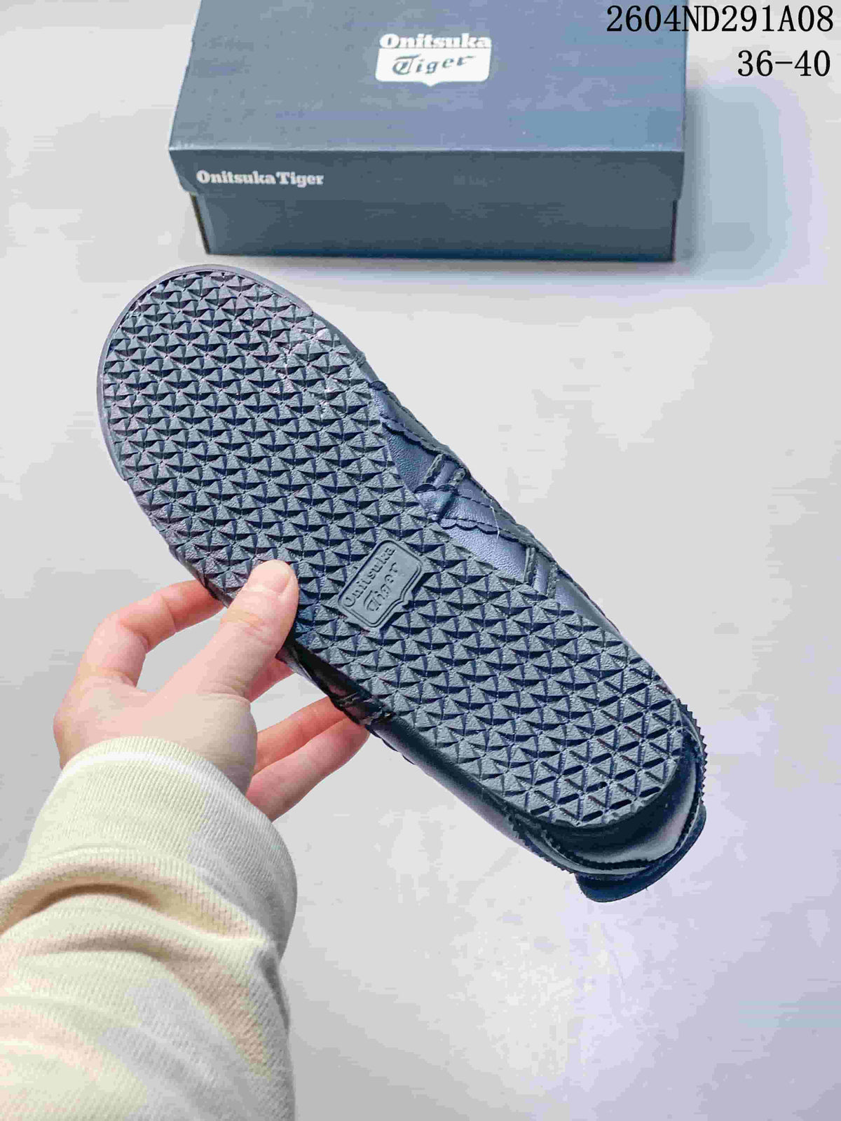 Underside of a black sneaker showing the textured rubber outsole and Onitsuka Tiger shoebox.