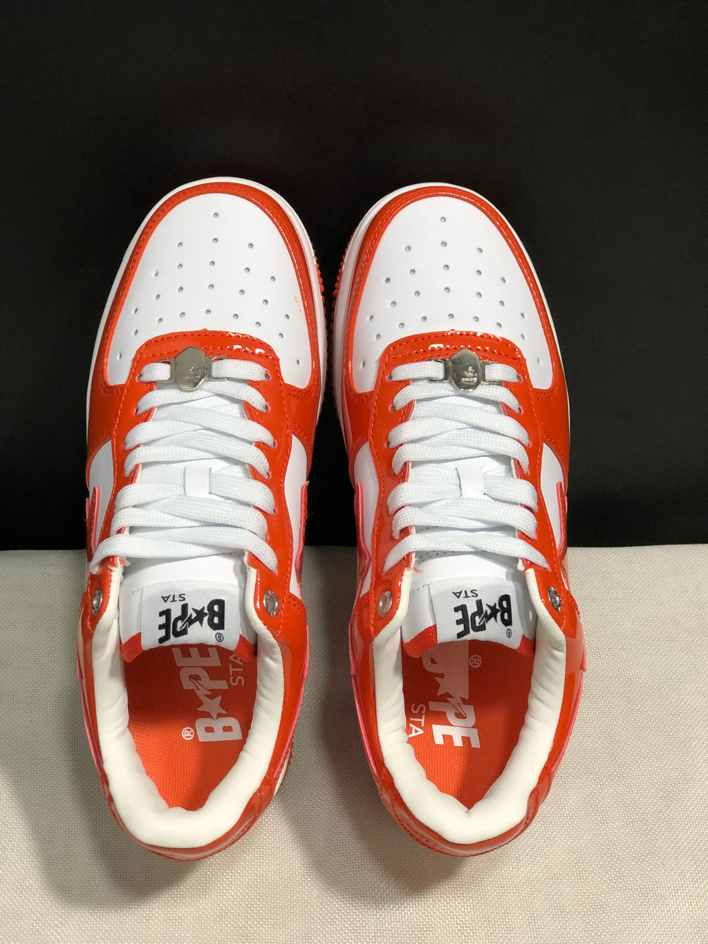 Top view of the pair showing white perforated toe boxes, orange overlays, white laces, and metal lace hardware.