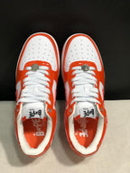 Top view of the pair showing white perforated toe boxes, orange overlays, white laces, and metal lace hardware.