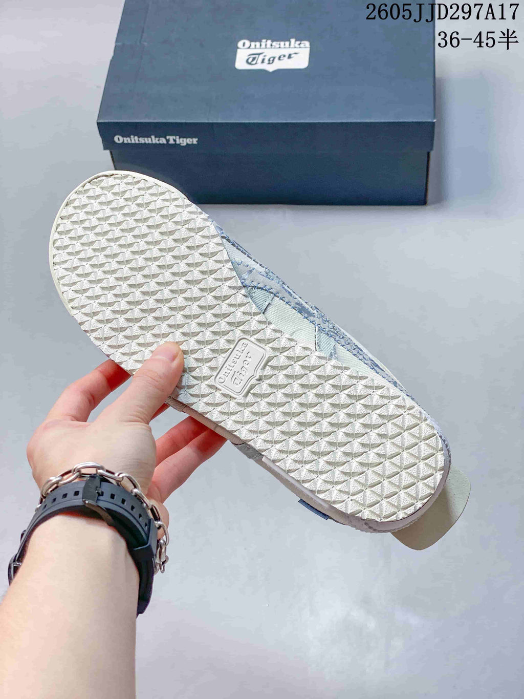 Underside view of an Onitsuka Tiger sneaker showing the repeating textured rubber outsole and branded shoebox; JJD297A17 and the size range 36–45.5 are visible.