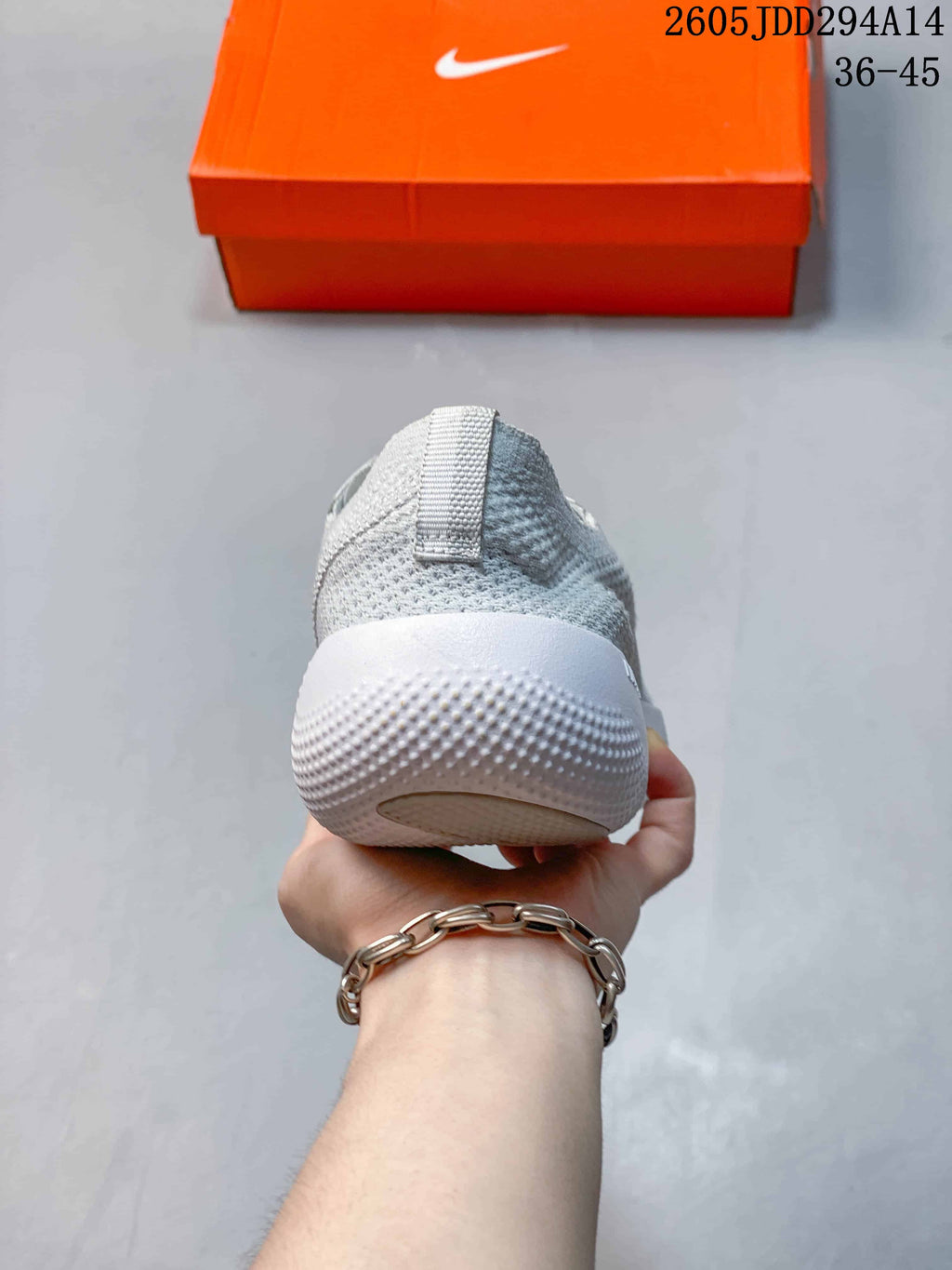 Rear view of the light gray knit sneaker showing the padded heel, pull tab, and textured white outsole.