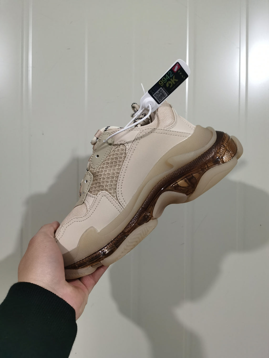 Close-up angled view of a nude Balenciaga Triple S sneaker showing layered panels, mesh detailing, laces, and a translucent brown-toned sole.
