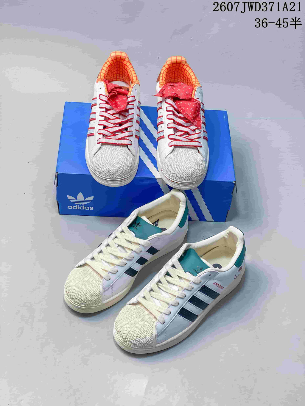 Two visible color versions of the white Adidas Superstar sneaker, one with red accents and one with dark blue and teal accents, shown with a blue Adidas shoebox; overlay states 2607TWD371A21 and sizes 36–45 with half sizes.