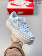Angled side view of the light blue and white sneaker showing the Swoosh, perforated toe and thick sole.