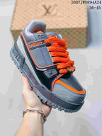 Angled side view of the gray and black Trainer Maxi sneaker with orange laces and trim.