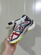 Side view of a Balenciaga Runner sneaker showing black, white and red layered panels with fluorescent yellow outsole accents.