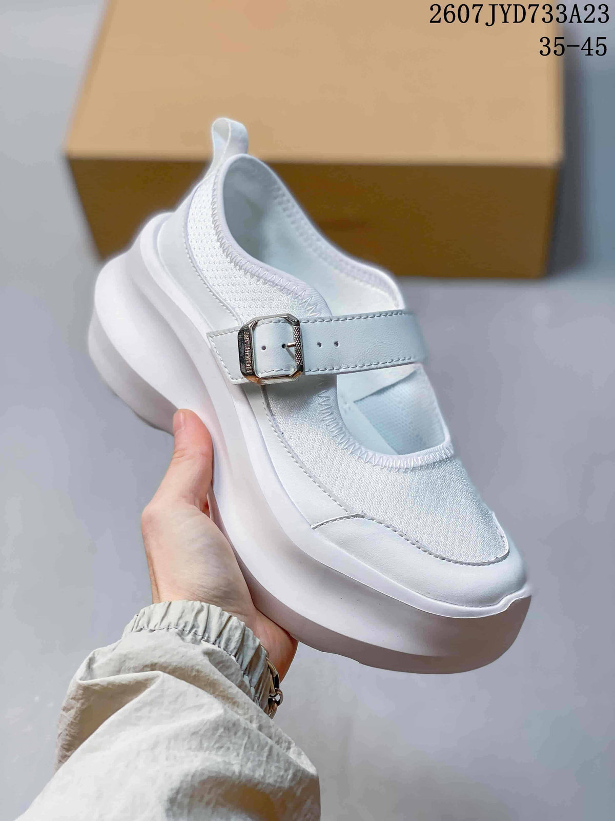 Three-quarter view of the white sneaker showing the buckle strap, textured upper panel, and thick platform sole.