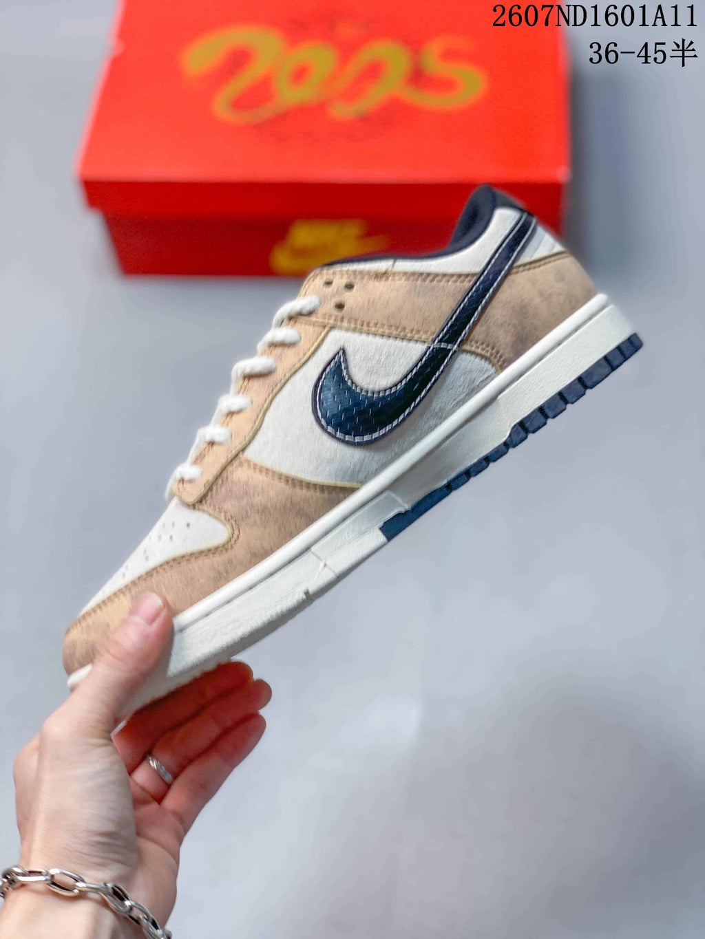 Side view of a low-top sneaker showing layered tan and white panels, a dark textured Swoosh, white midsole, and navy outsole.