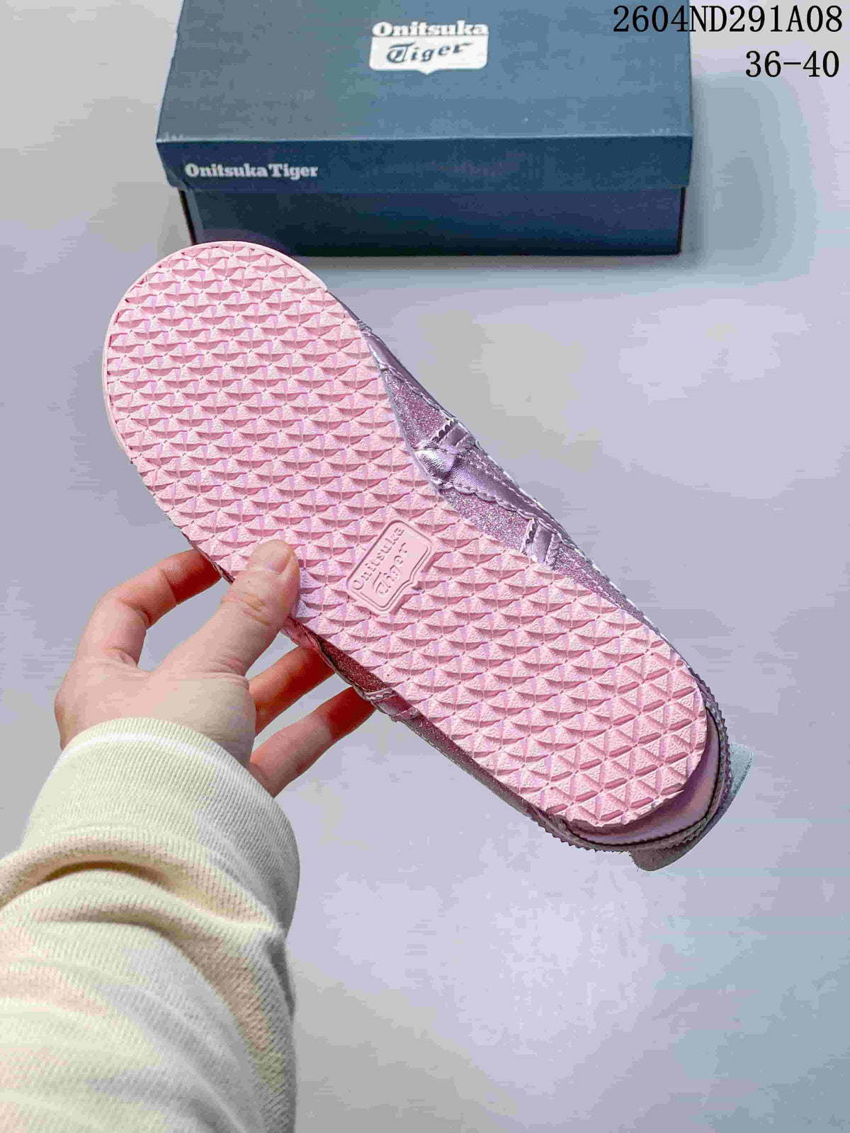 Underside of a pink sneaker showing the repeating textured outsole pattern and Onitsuka Tiger branding.