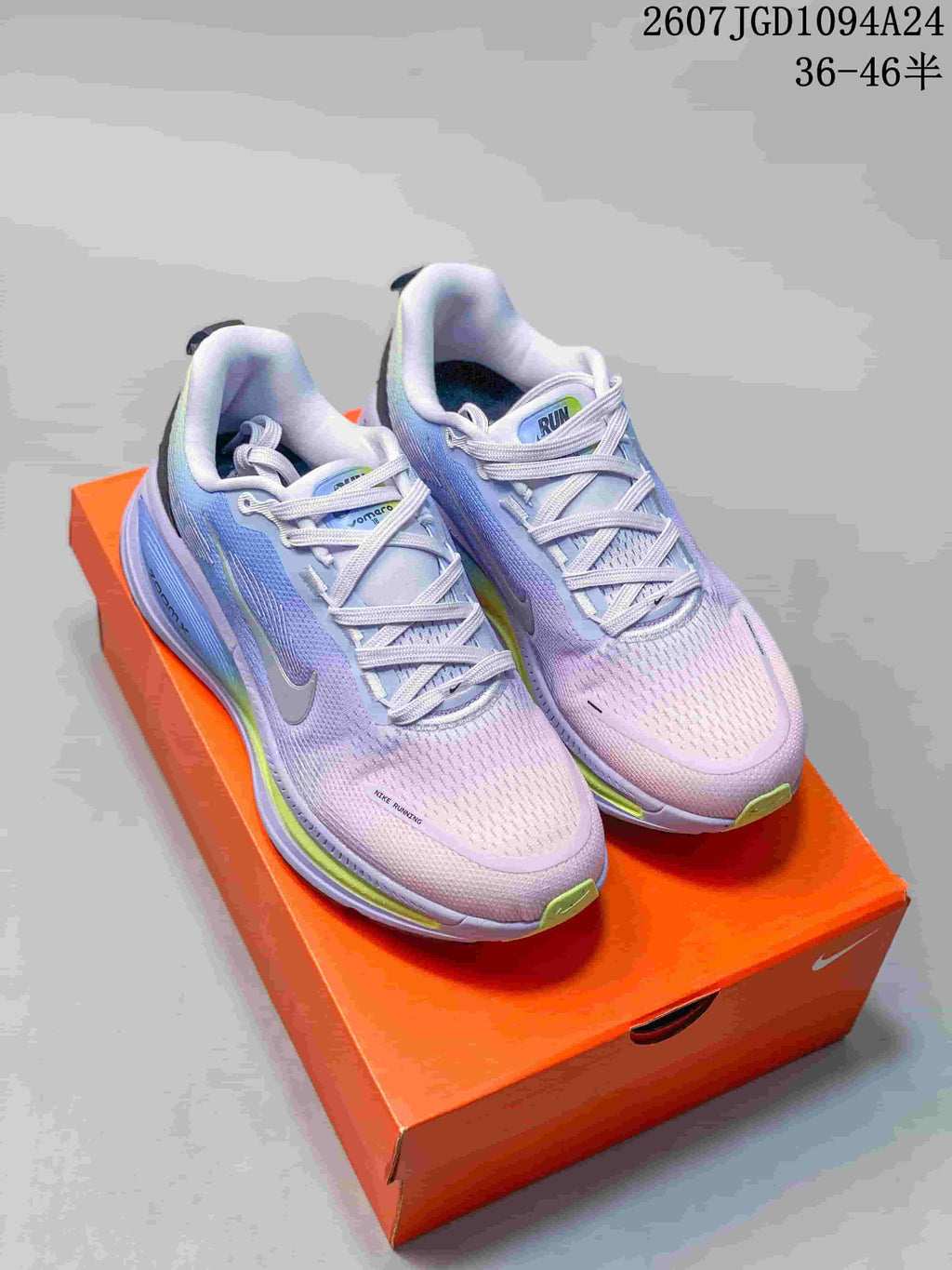 Pair of lavender and blue Nike Vomero 18 SE sneakers displayed on an orange shoebox.