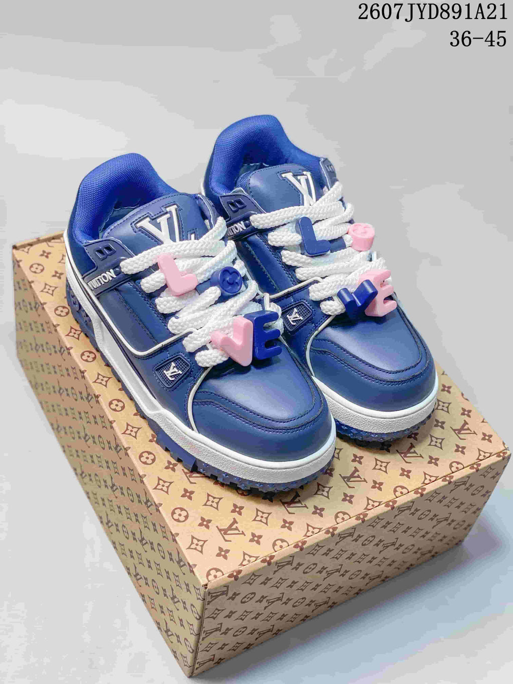 Pair of blue Louis Vuitton Trainer Maxi sneakers displayed on a patterned shoe box, showing white laces, decorative lace charms, and the blue-and-white sole.