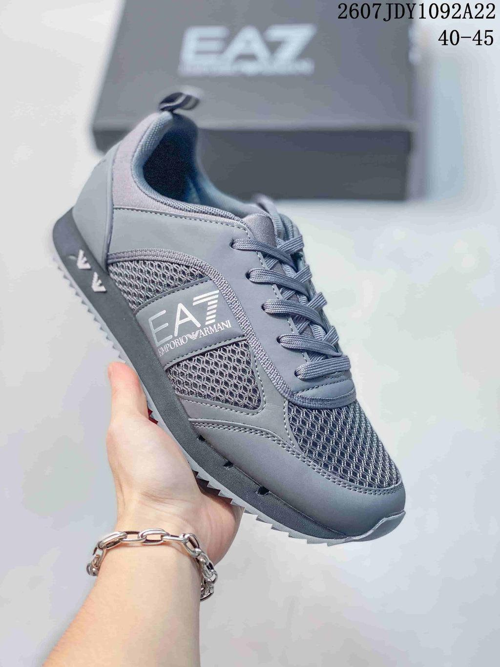 Angled side view of the gray EA7 sneaker showing the side branding, mesh panels, lace-up front, and textured outsole.