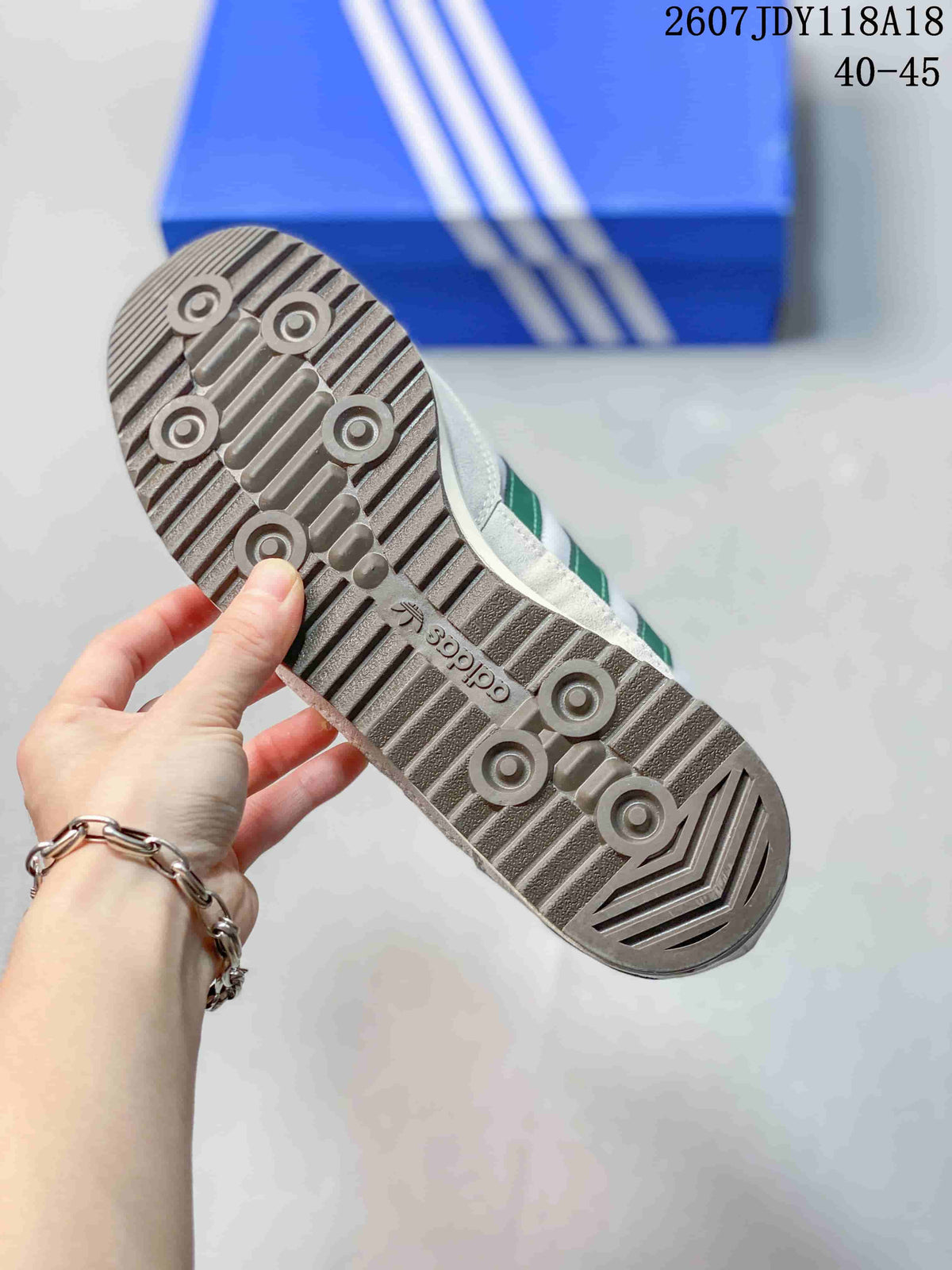 Underside of the sneaker showing a grey textured rubber outsole with circular traction details and adidas branding.