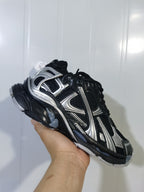 Close-up angled view of the black and silver Nike Runner sneaker showing its lace-up upper, mesh-style panels, silver overlays, and sculpted sole.