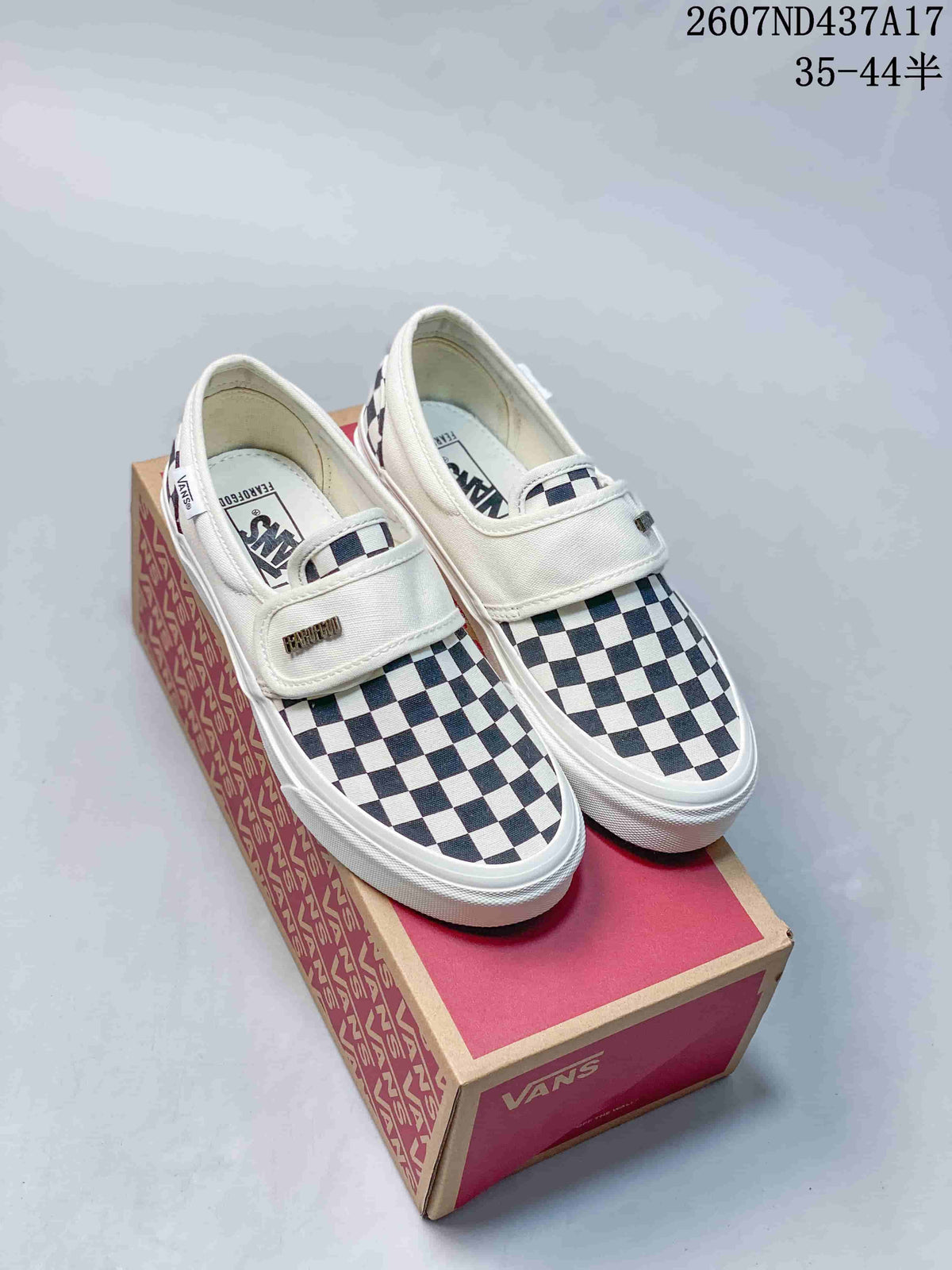 Pair of black-and-white checkerboard Vans slip-on sneakers with white straps and white rubber soles, shown on a Vans shoebox.
