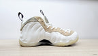 Side view of a white Air Foamposite One sneaker with sculpted panels, marbled beige trim, and a black pull tab.