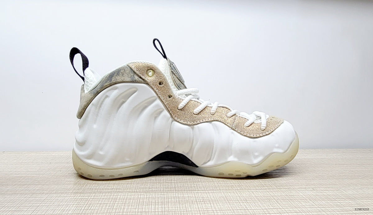 Side view of a white Air Foamposite One sneaker with sculpted panels, marbled beige trim, and a black pull tab.