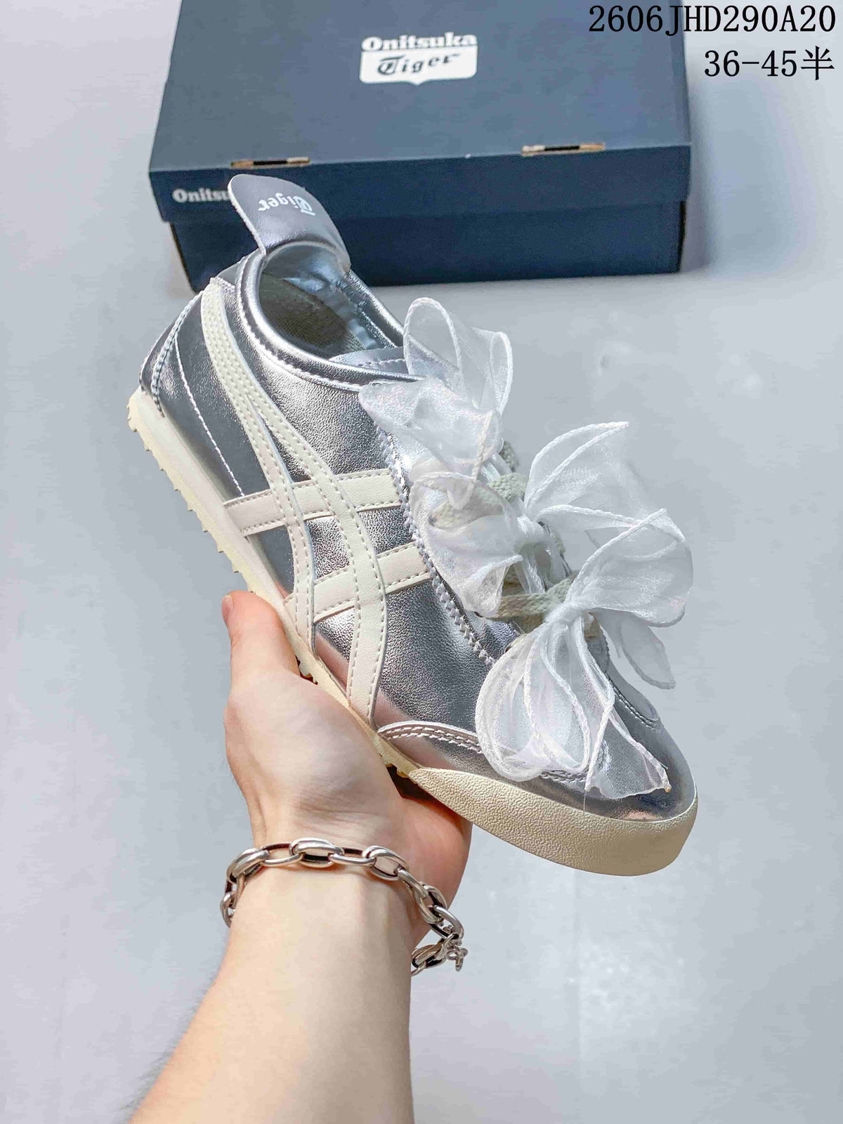 Angled side view of a silver sneaker with cream stripes and sheer bow laces.