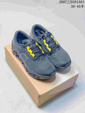 Pair of dark grey On Cloudmonster 3 LightSpray shoes with yellow lace accents, shown on a box.