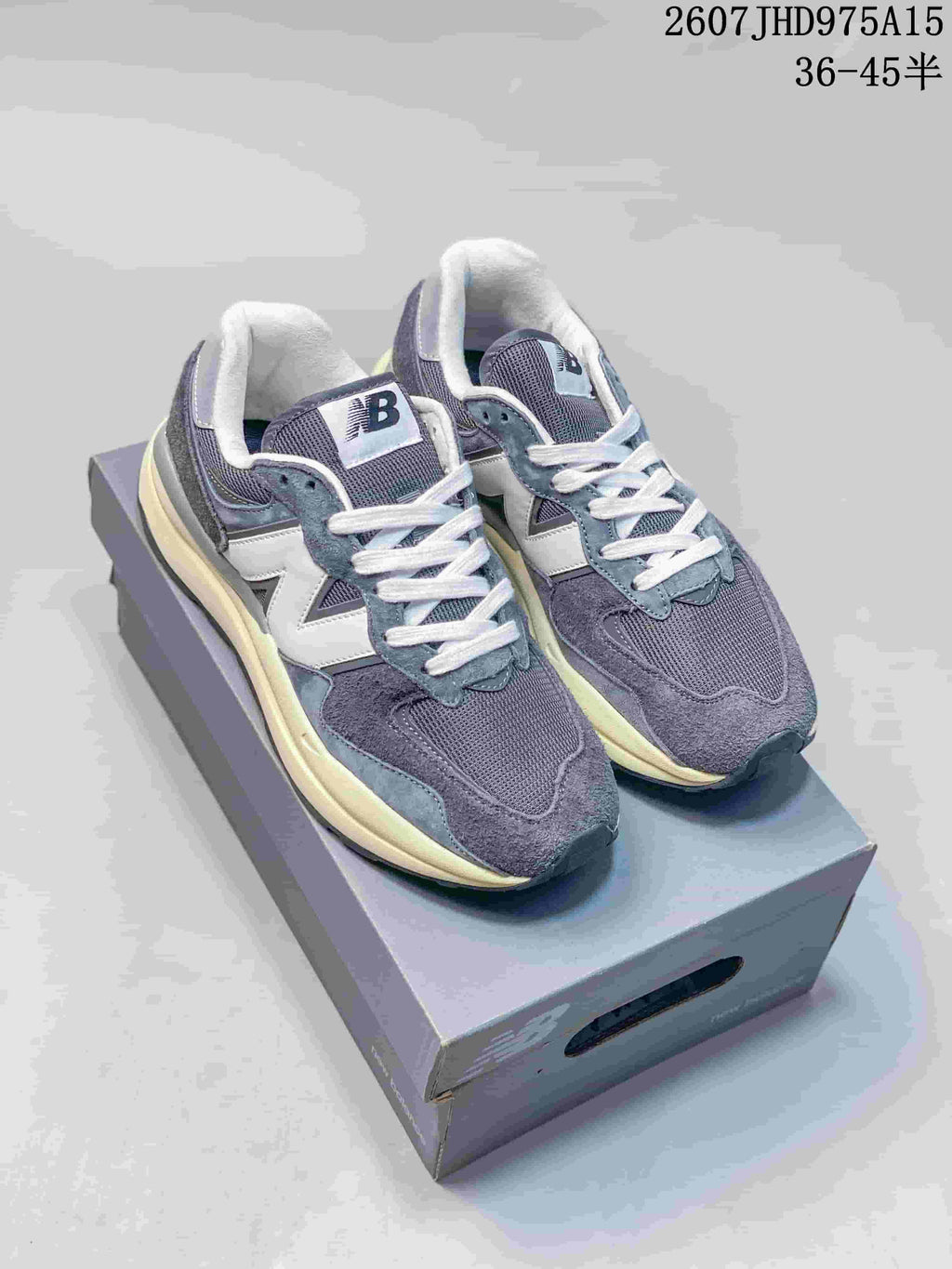 Pair of grey and white New Balance 5740 sneakers displayed on a shoebox, showing the layered upper and cream-colored midsole.