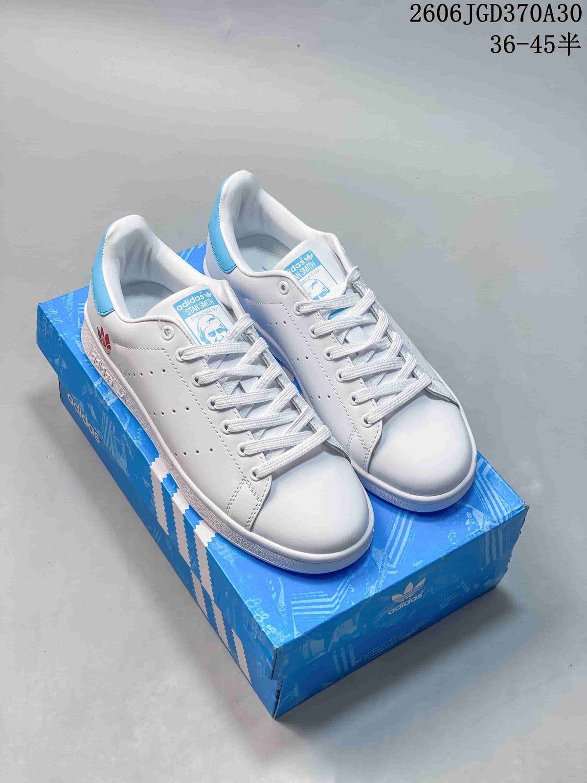 Pair of white Adidas Stan Smith sneakers with light-blue accents, pictured on a blue shoe box