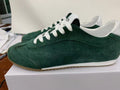 Side view of green Alo low-top sneakers with white laces, white accents, and a brown outsole on a box.