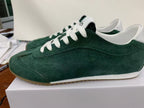 Side view of green Alo low-top sneakers with white laces, white accents, and a brown outsole on a box.