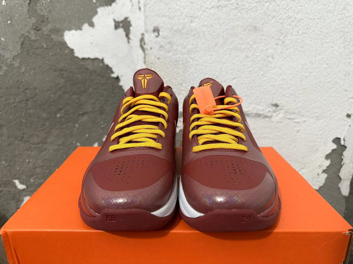 Front view of burgundy Nike Kobe basketball shoes with yellow laces and gold tongue logos