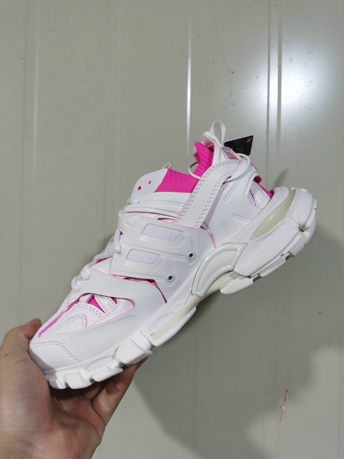 Rear and side view of the white and fluorescent pink sneaker, showing the structured heel, layered panels and segmented sole.
