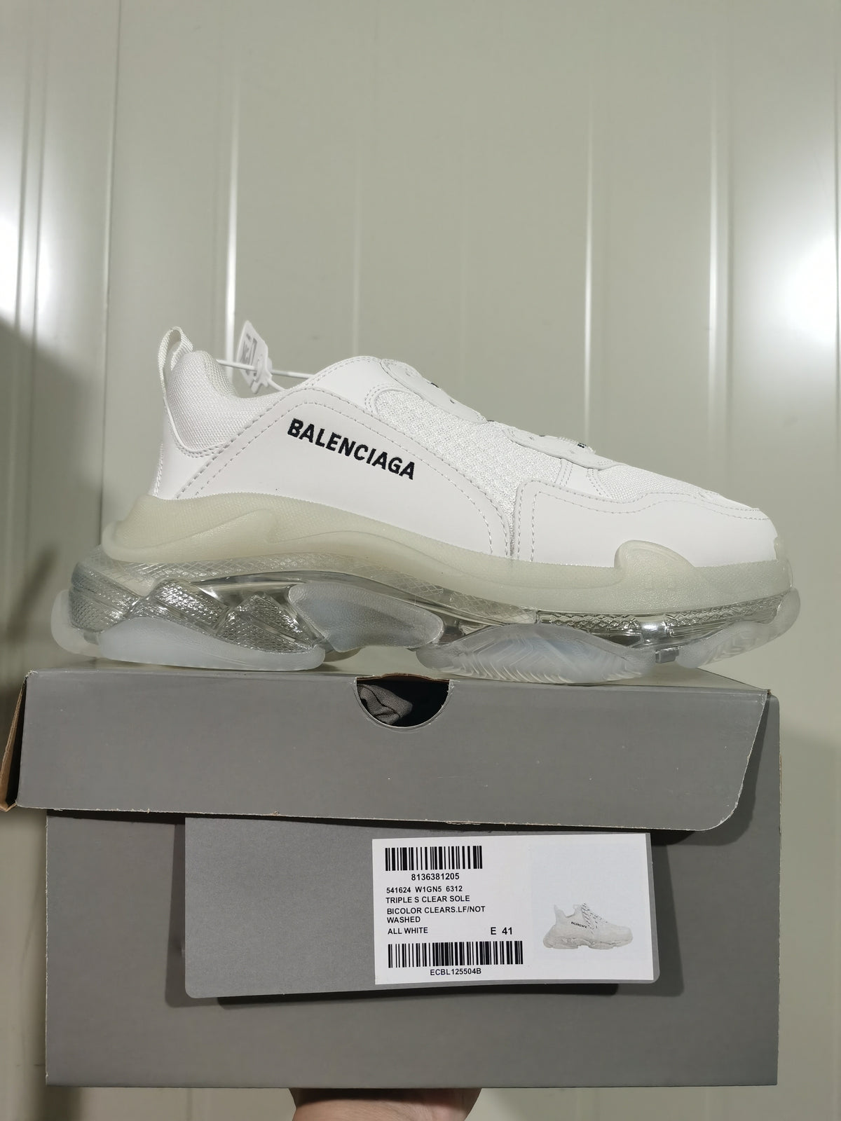 White Balenciaga Triple S sneaker displayed on its box; the box label shows Triple S Clear Sole, all white, and EU size 41.