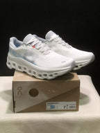 Pair of ivory and glacier On Cloudmonster 1 running shoes displayed on a branded shoe box; the box label shows EU 38 for the photographed sample.