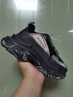 Close-up side view of a black and grey Balenciaga sneaker showing layered panels, textured detailing, sculpted sole, and side branding.