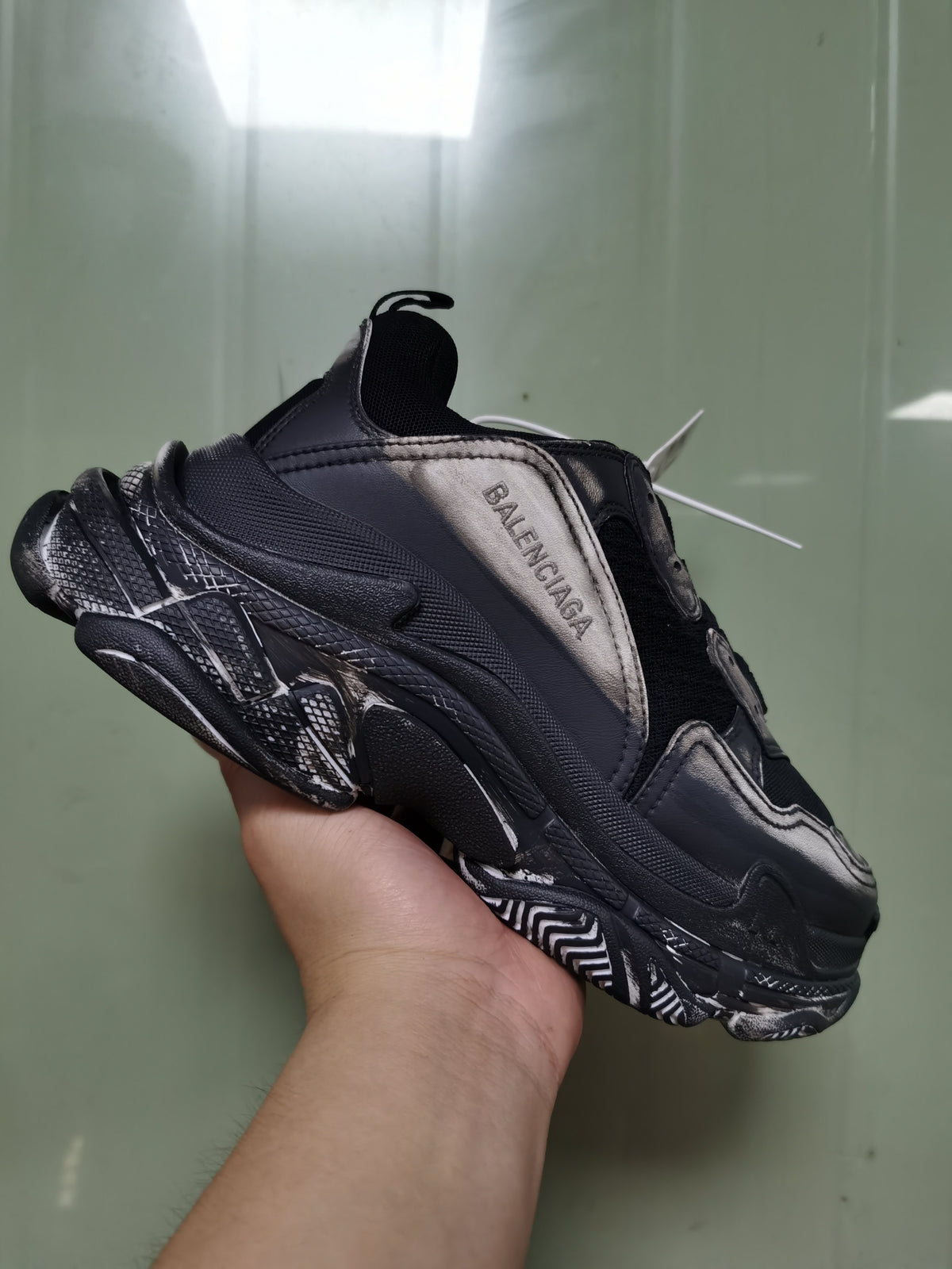Close-up side view of a black and grey Balenciaga sneaker showing layered panels, textured detailing, sculpted sole, and side branding.