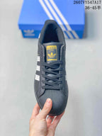 Top view of the sneaker showing black laces, gold-tone tongue branding and a textured shell-style toe.