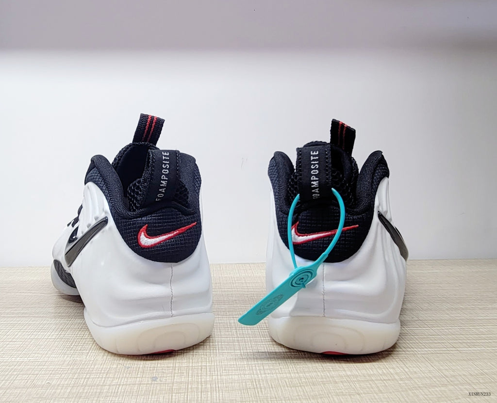 Rear view of white Nike Air Foamposite One sneakers with black collars and red heel logo accents