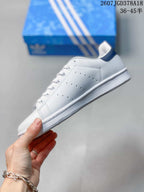 Side view of a white low-top sneaker with perforated panel details and a navy heel accent.