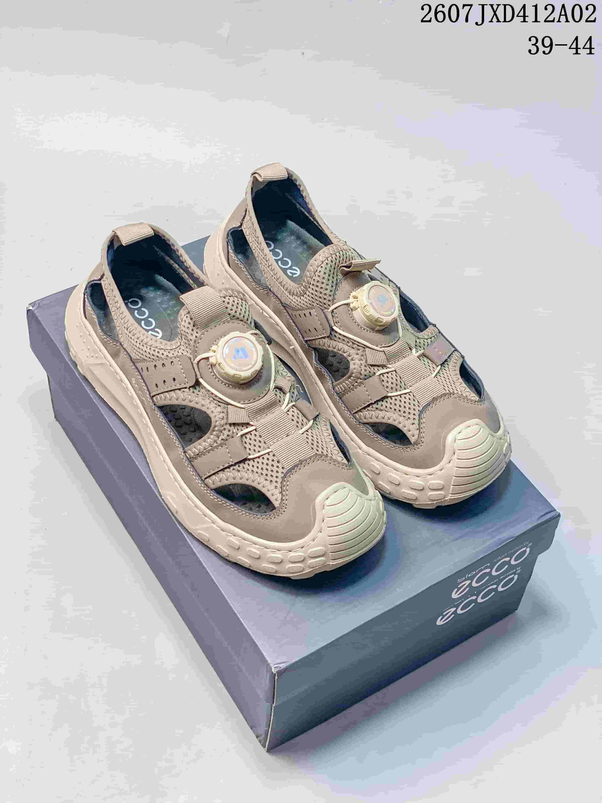 Pair of taupe closed-toe outdoor sandals with dial-style fastenings, shown on a box; image states sizes 39–44.