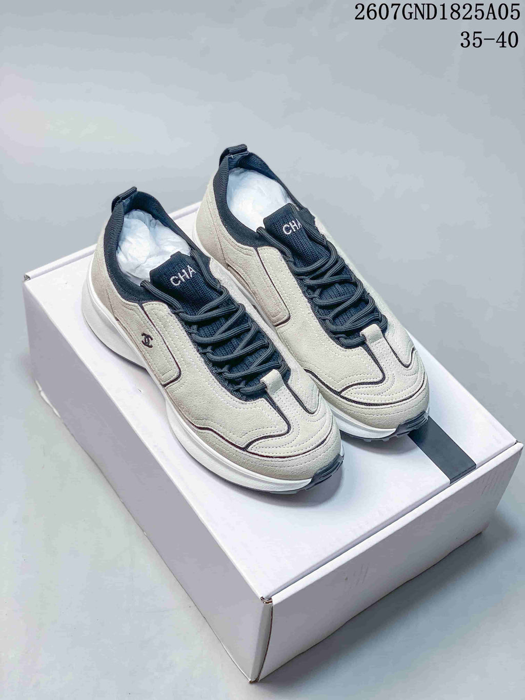 Pair of off-white and dark Chanel sneakers displayed on a white shoebox.