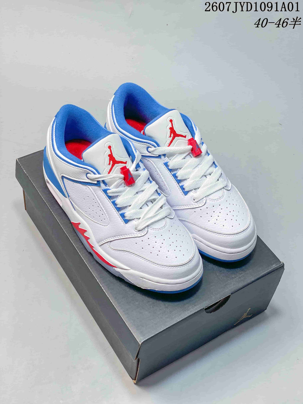 Pair of white Jordan low-top sneakers with blue and red details, shown on a dark shoebox